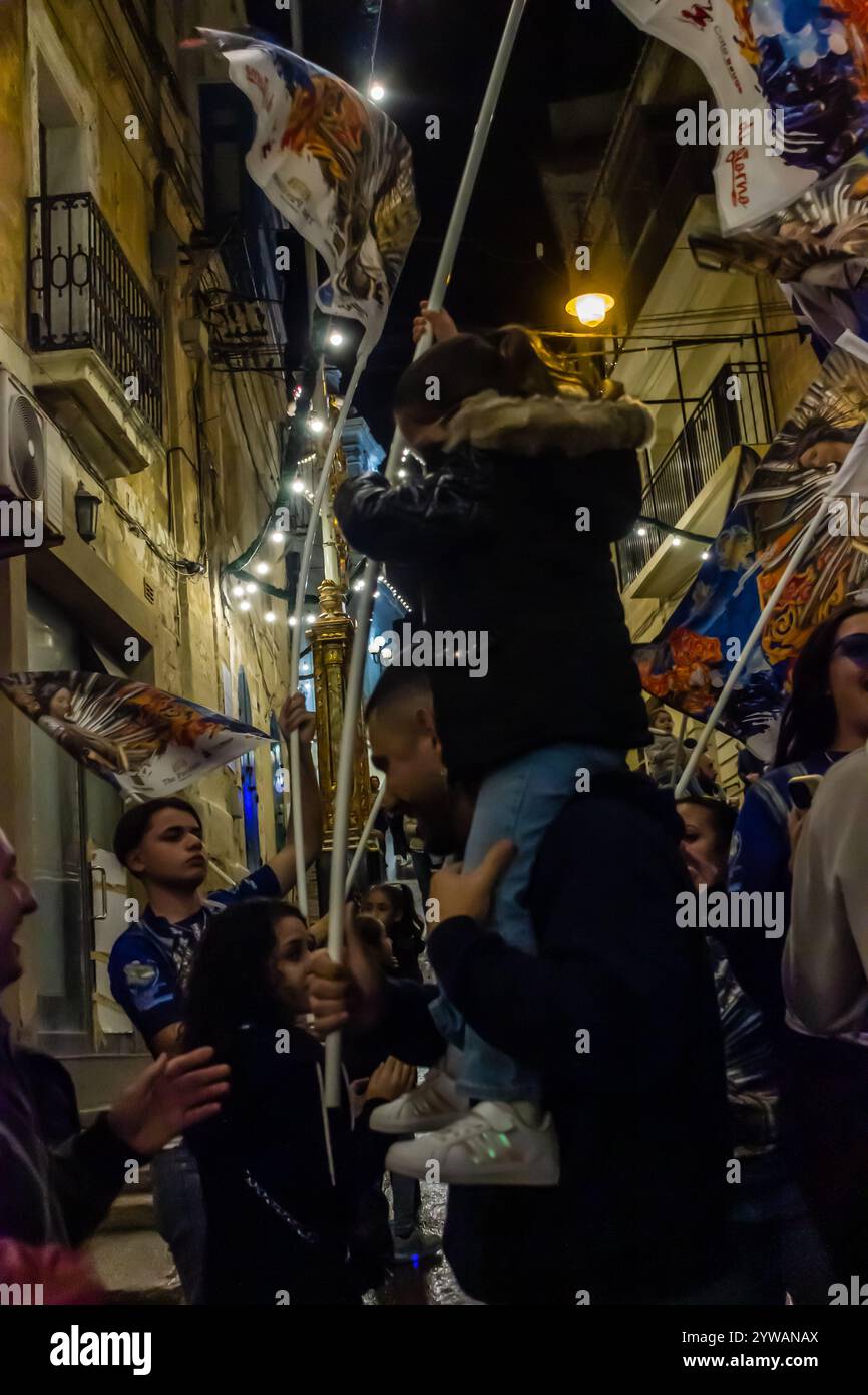 Cospicua, Malta - 6 dicembre 2024. Festa notturna eccitata con bandiere colorate e folla entusiasta Foto Stock