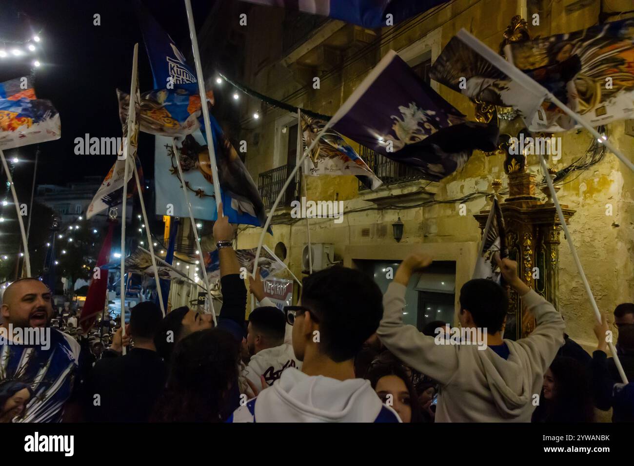 Cospicua, Malta - 6 dicembre 2024. Festa notturna eccitata con bandiere colorate e folla entusiasta Foto Stock