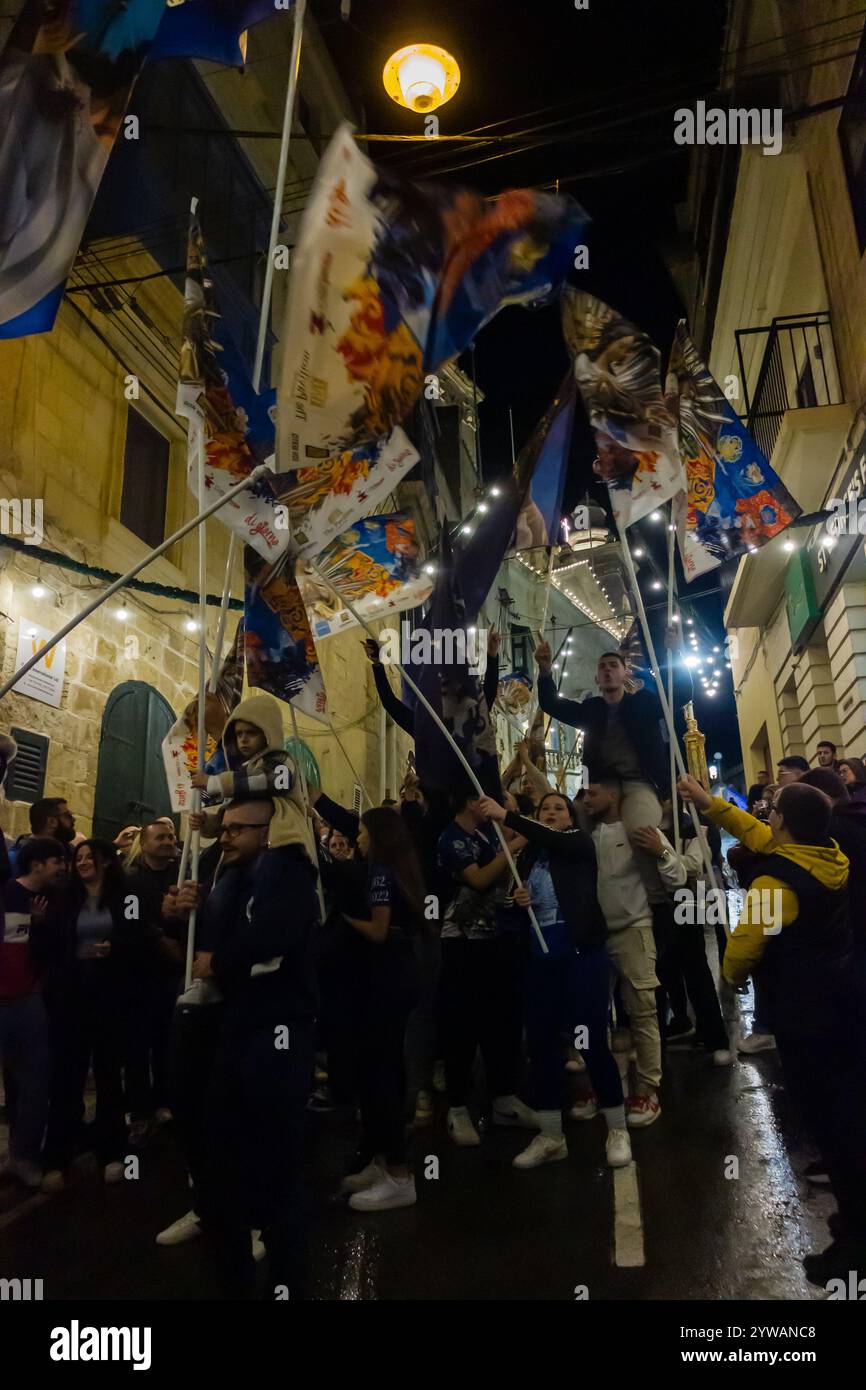 Cospicua, Malta - 6 dicembre 2024. Festa notturna eccitata con bandiere colorate e folla entusiasta Foto Stock