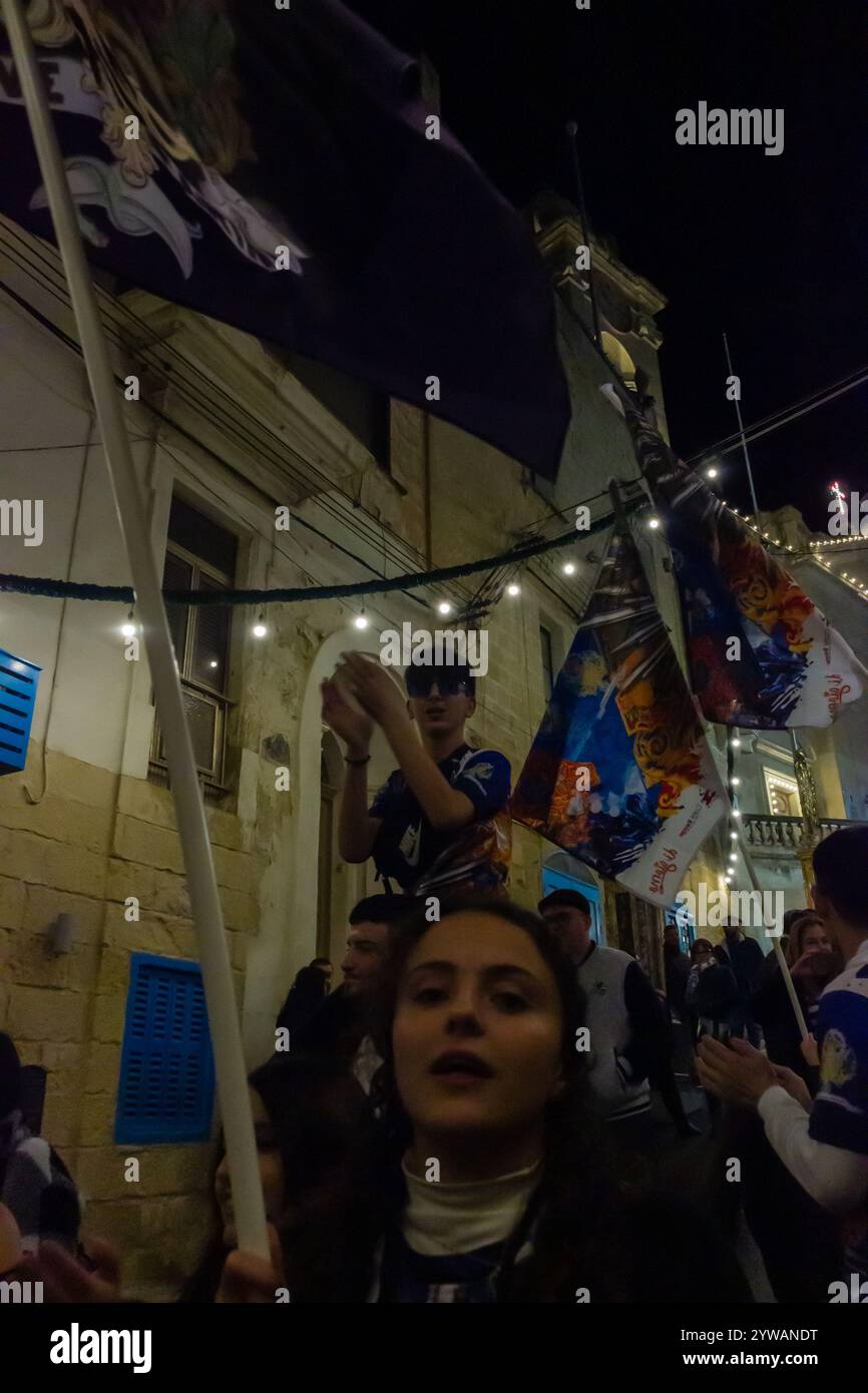 Cospicua, Malta - 6 dicembre 2024. Festa notturna eccitata con bandiere colorate e folla entusiasta Foto Stock