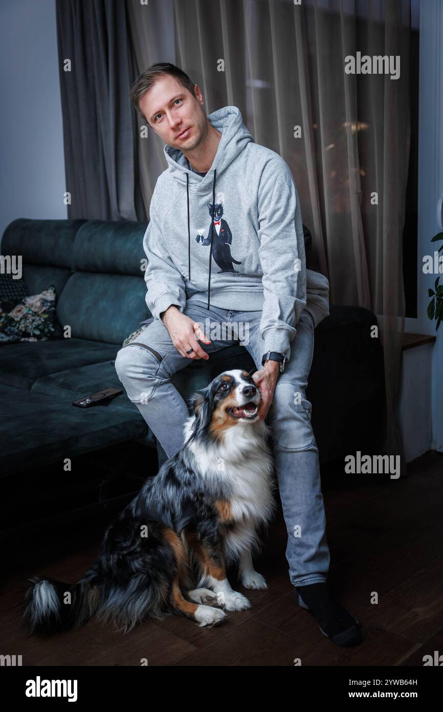 Giovane uomo e pastore australiano nell'accogliente ambiente del soggiorno Foto Stock