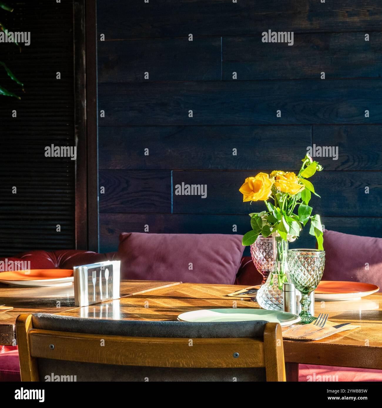 rose gialle fresche in vaso di vetro illuminato dalla luce del sole sul tavolo del ristorante Foto Stock