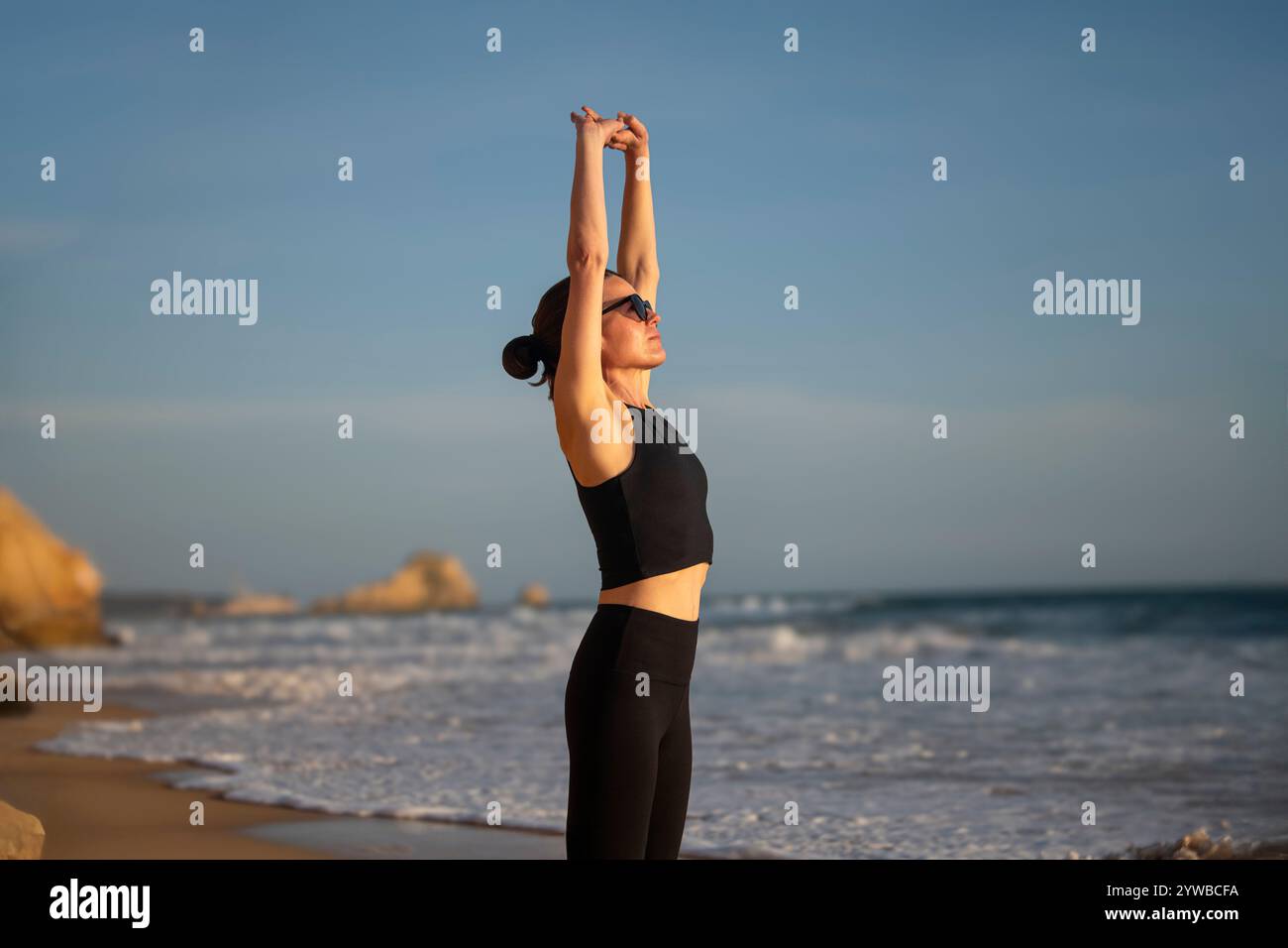 donna sportiva con le braccia sopra la testa che si allunga sulla spiaggia al sole Foto Stock