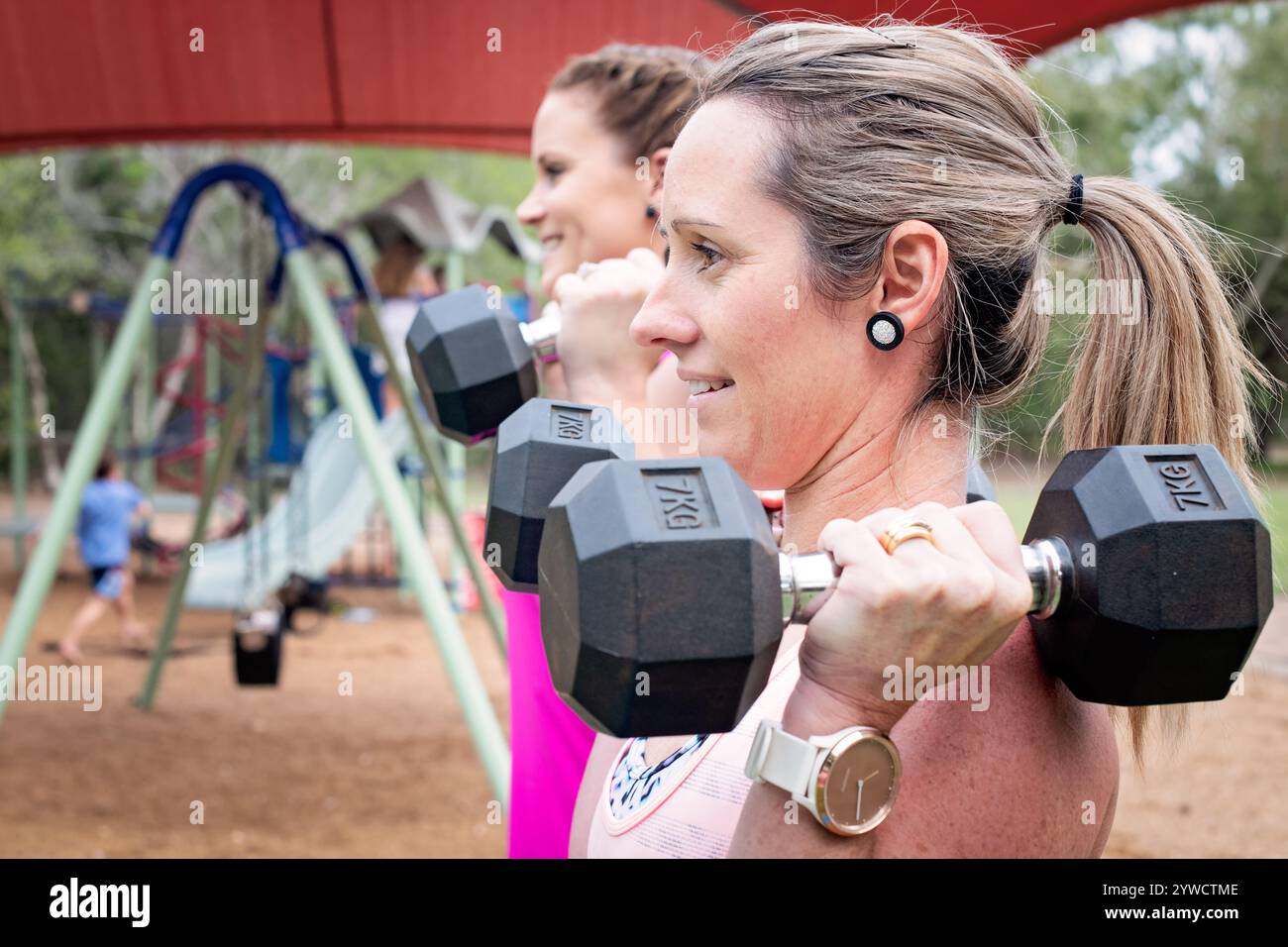 due donne che sollevano pesi manubri, parco all'aperto, stile di vita sano, mamma mamma impegnata, personal trainer, fitness divertente con amici, supporto alla motivazione Foto Stock