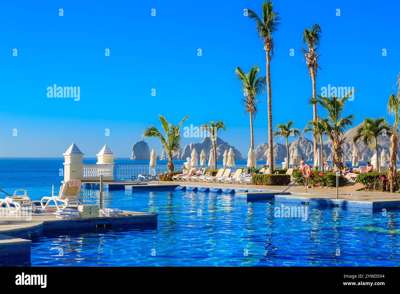 Una bellissima piscina con palme e ombrelloni. La piscina è circondata da sedie e ombrelloni e ci sono persone che si godono la vista. La scena e' relax Foto Stock