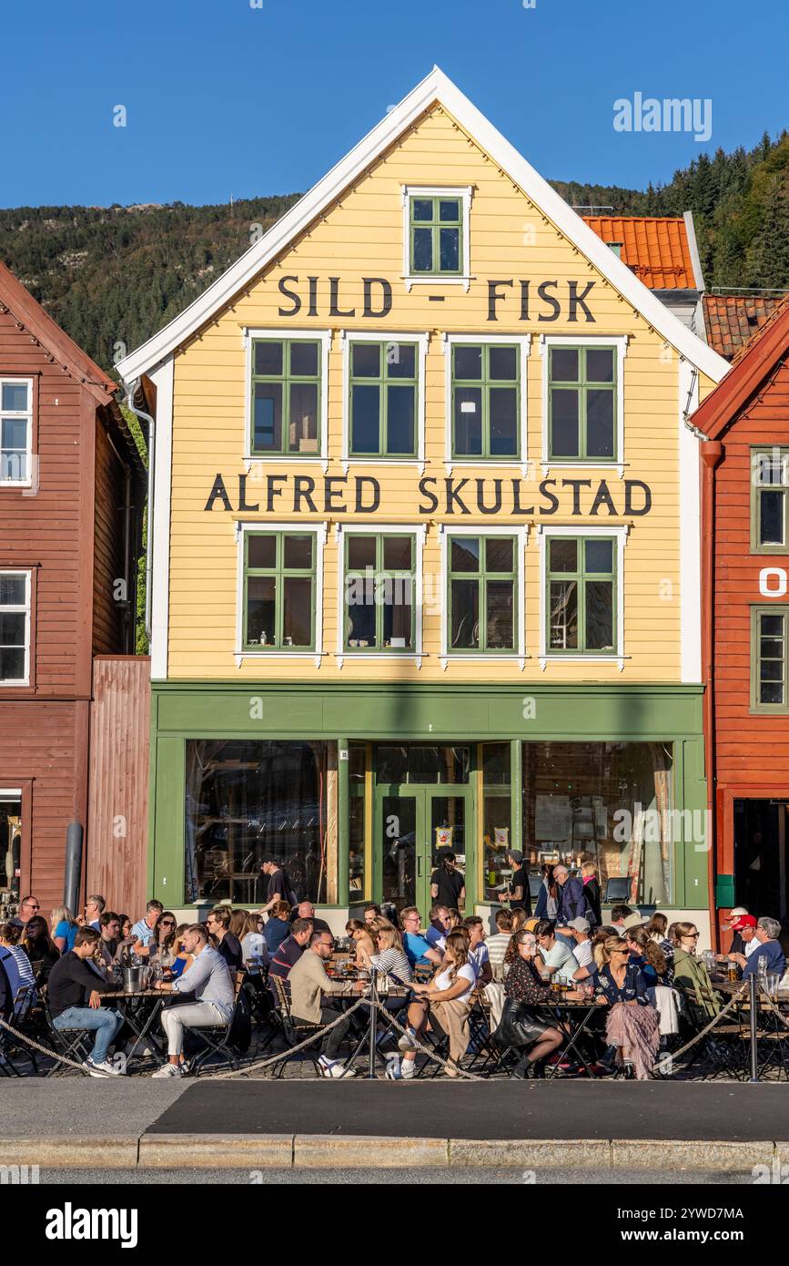 Bryggen, patrimonio dell'umanità dell'UNESCO, nel centro di Bergen, con bar e pub che ospitano amici che socializzano all'esterno, Bergen, Norvegia, Europa, 2024 Foto Stock