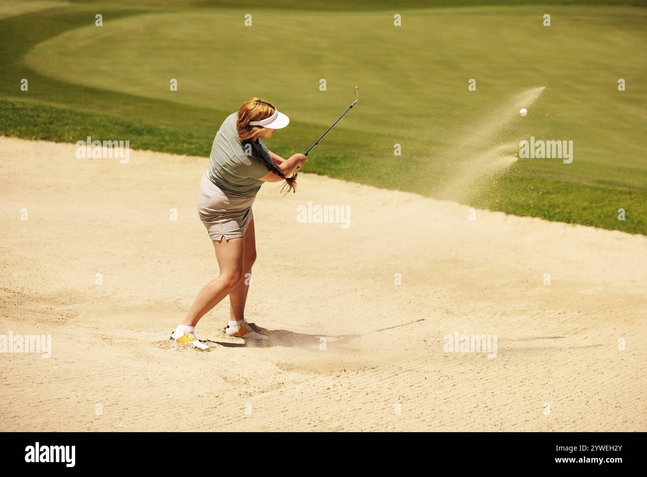 Una golfista dilettante colpisce sapientemente una palla da golf da un bunker, mostrando concentrazione e tecnica in una giornata luminosa e soleggiata al campo da golf. Foto Stock