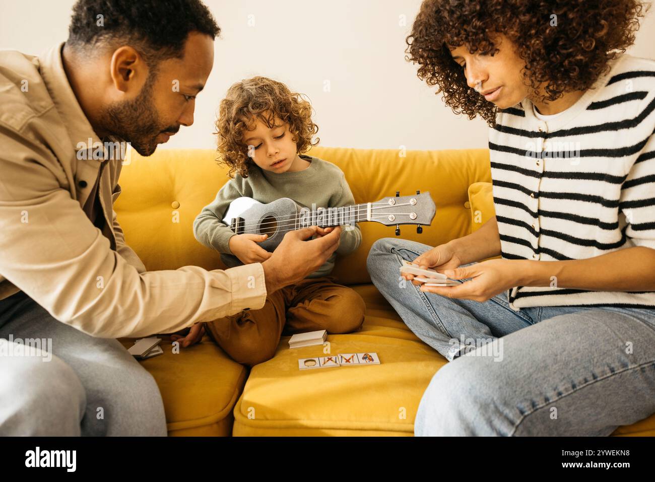 Una famiglia che si diverte a trascorrere momenti di qualità insieme mentre gioca a musica e giochi di carte su un divano giallo. Foto Stock