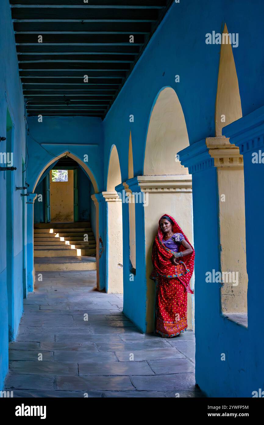 Donna locale in sari rossi sotto l'arco di un palazzo storico a Poshina, in India Foto Stock