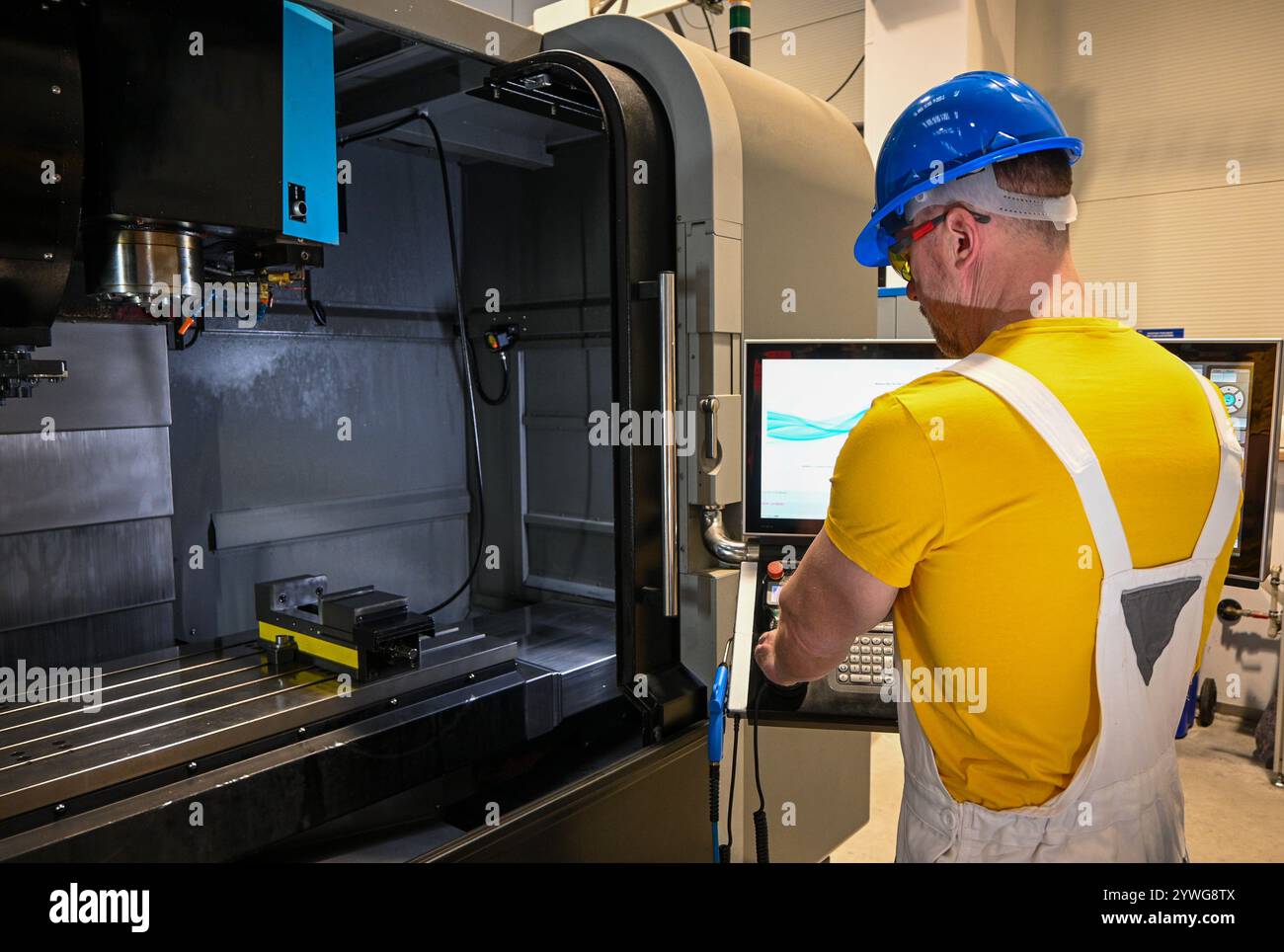 Lavoratore di metalli che indossa occhiali di sicurezza e elmetto utilizzando una fresatrice cnc in officina. Foto Stock