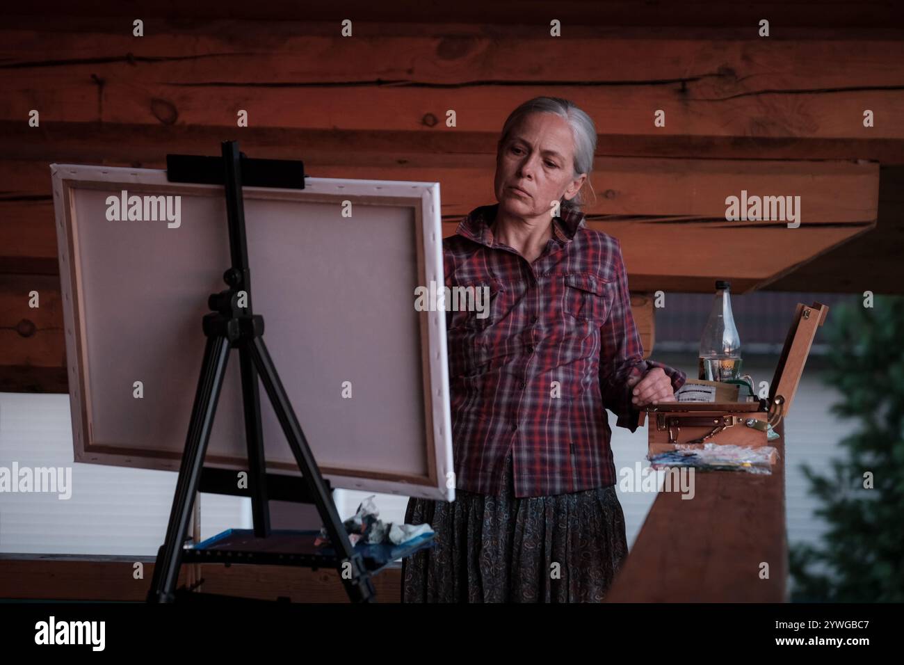 Una donna sta dipingendo un quadro su una tela. Indossa una camicia a quadri e una gonna Foto Stock