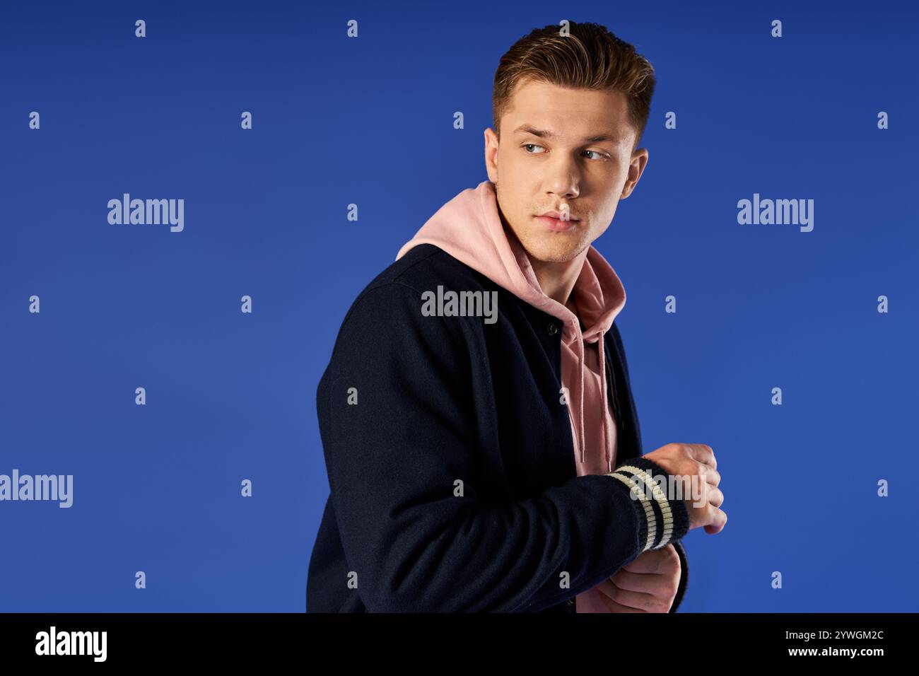 Un giovane uomo che indossa un abbigliamento casual mostra fiducia mentre si trova di fronte a uno sfondo blu. Foto Stock