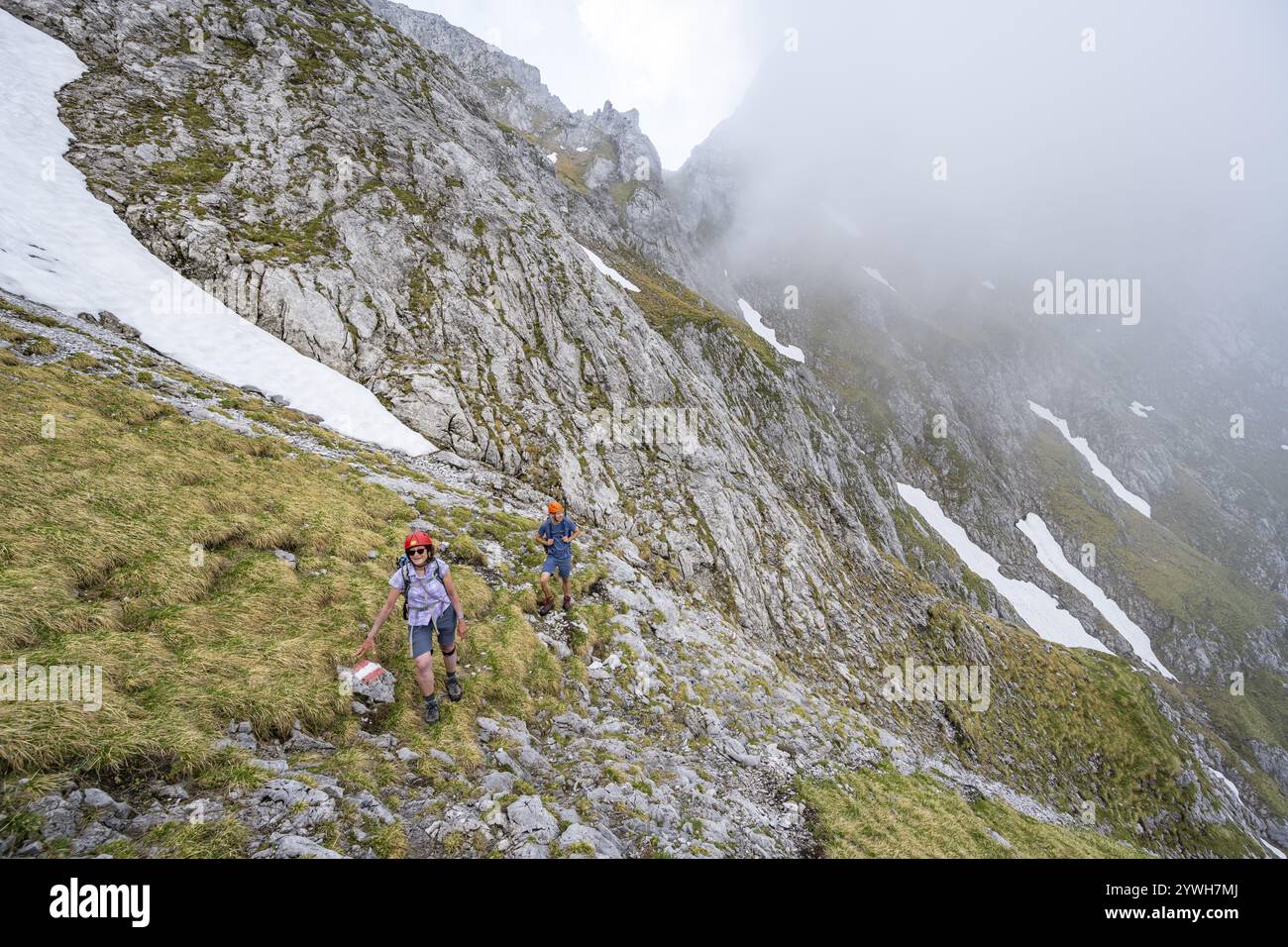 Alpinista con casco su uno stretto sentiero escursionistico, ascesa all'Ackerlspitze, nuvole che si muovono intorno alle montagne, Wilder Kaiser, Kaiser Mountains, Tyr Foto Stock
