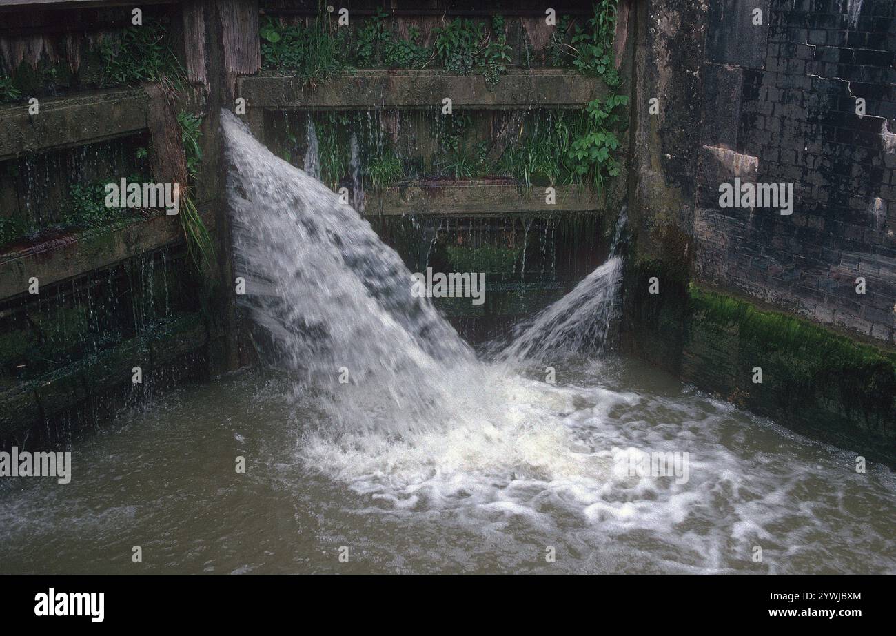L'acqua del canale scorre attraverso i cancelli di blocco: Una fredda giornata grigia a maggio a Stockton Locks Canal l'acqua passa attraverso uno spazio all'interno dei cancelli di blocco. Il volo di Stockton con 10 chiuse si trova sul Grand Union Canal vicino allo storico villaggio di Stockton nel Warwickshire. Dalle chiuse si possono ammirare splendide vedute della campagna circostante. Stockton Top Marina e il Boat Inn sono in cima al volo e il pub Blue Lias è in fondo. Il Grand Union Canal collega Londra e Birmingham ed è stato completato all'inizio del XIX secolo. Le chiuse di Stockton si trovano tra Napton Junction e il villaggio di Long Itchington. Foto Stock