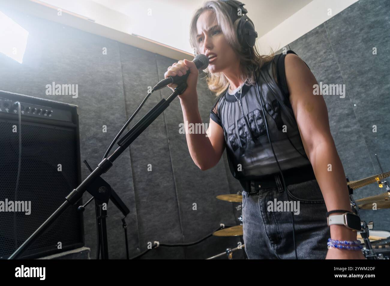 Cantante femminile che registra la voce in uno studio di musica professionale. Donna in cuffie che canta nel microfono tra le apparecchiature da studio. Produzione musicale, performance e registrazione. Foto Stock