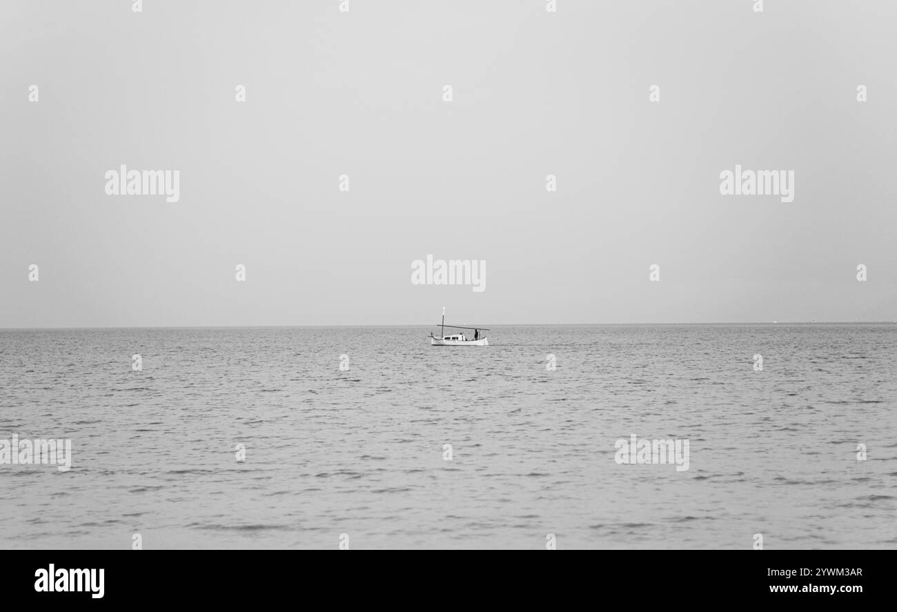 Piccola barca da pesca bianca solitaria nel mare calmo. Foto minimalista a tema marino, adatta per l'uso come carta da parati, sul sito web, per decorazioni interne Foto Stock