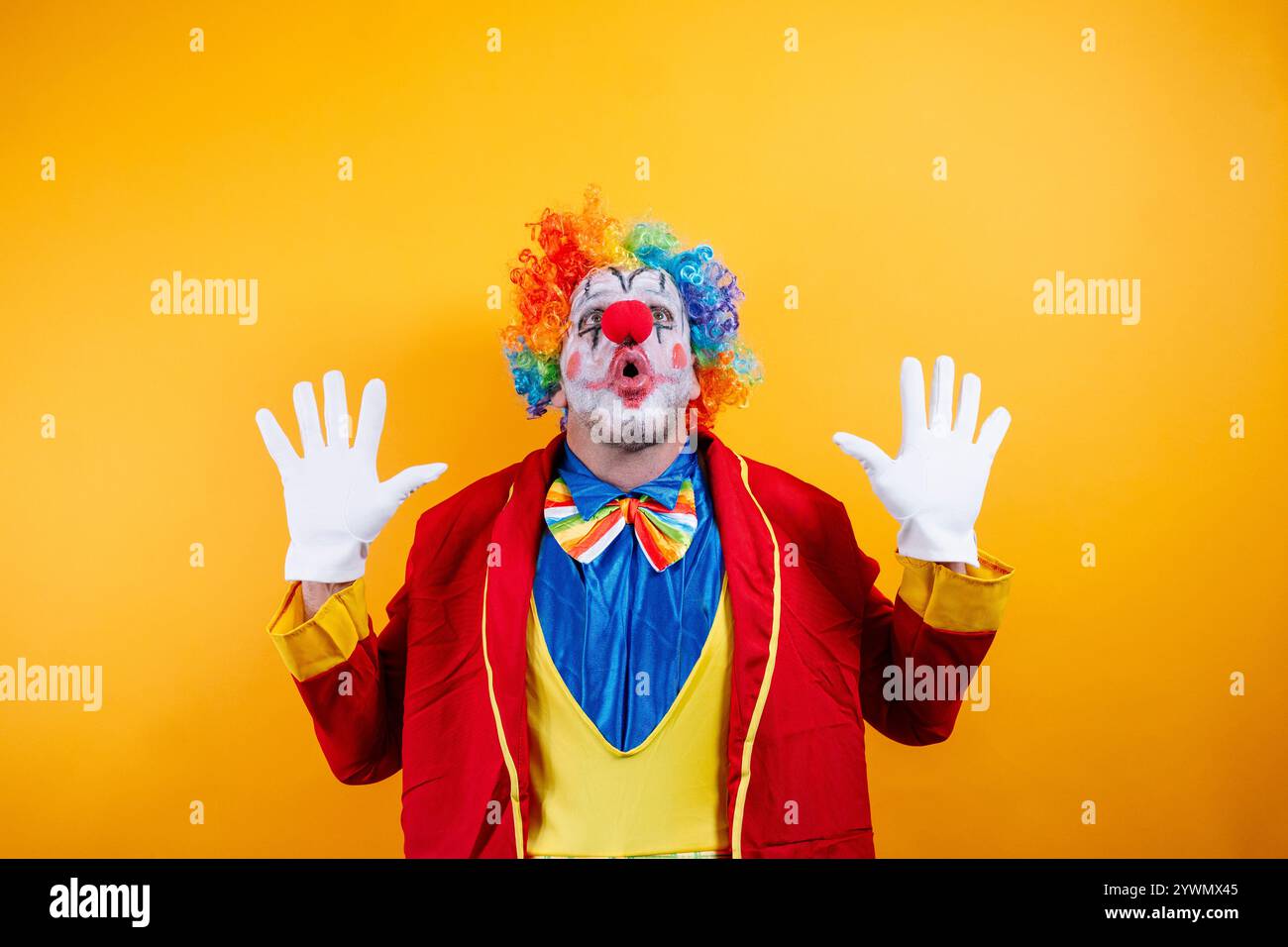 Clown scioccato con parrucca arcobaleno, occhi larghi, mani in alto Foto Stock