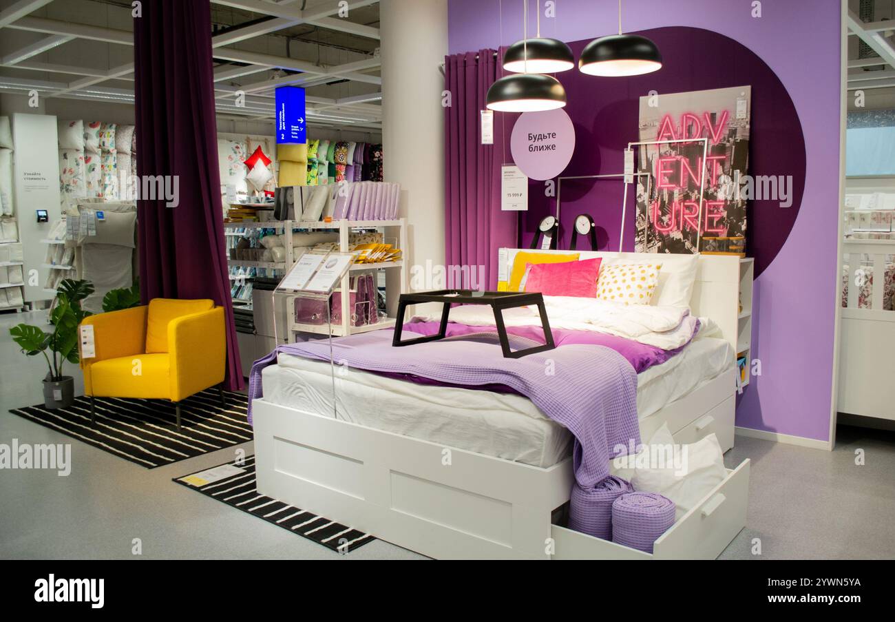 Mosca, Russia, settembre 2019: Camera da letto con pareti viola, biancheria bianca, cuscino rosa e un motivo di pois gialli. Orologi neri e posizione foto Foto Stock