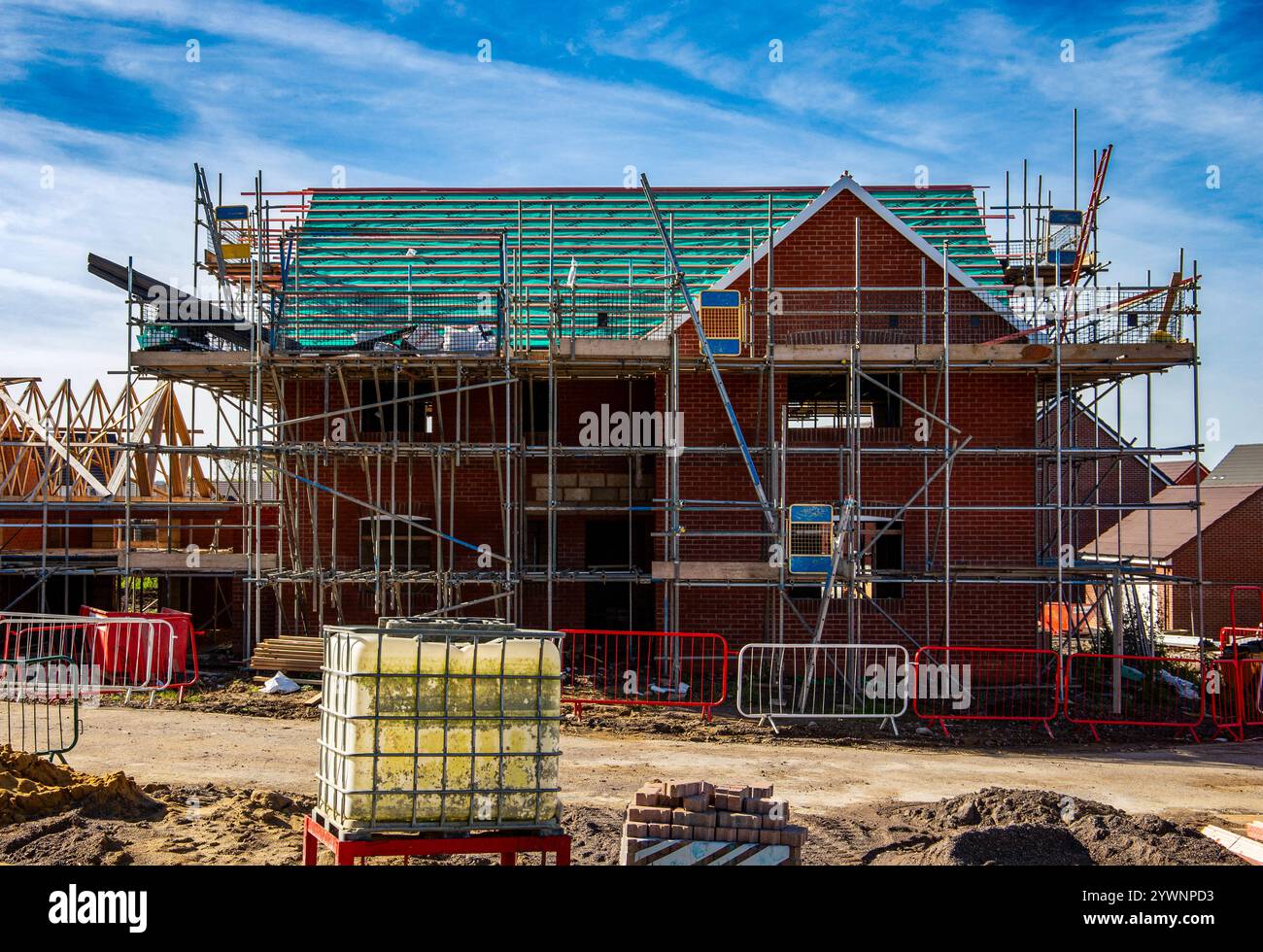Ponteggi intorno a una nuova casa costruita in un complesso residenziale con attrezzature da cantiere tutto intorno Foto Stock