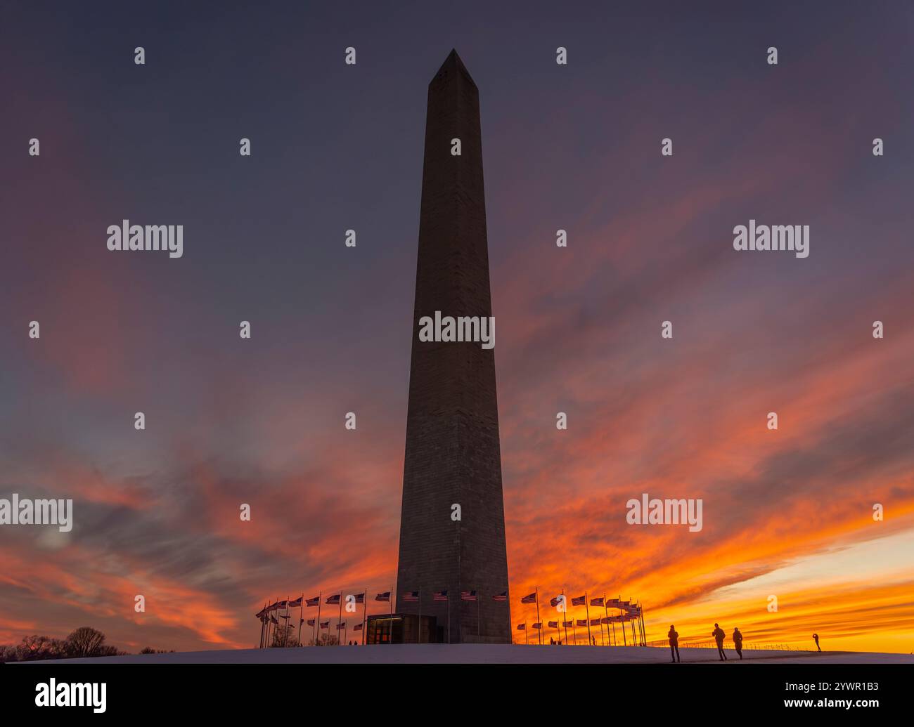 Il monumento a Washington al tramonto si staglia contro un drammatico cielo arancione e rosa, con bandiere statunitensi che circondano la base. Foto Stock