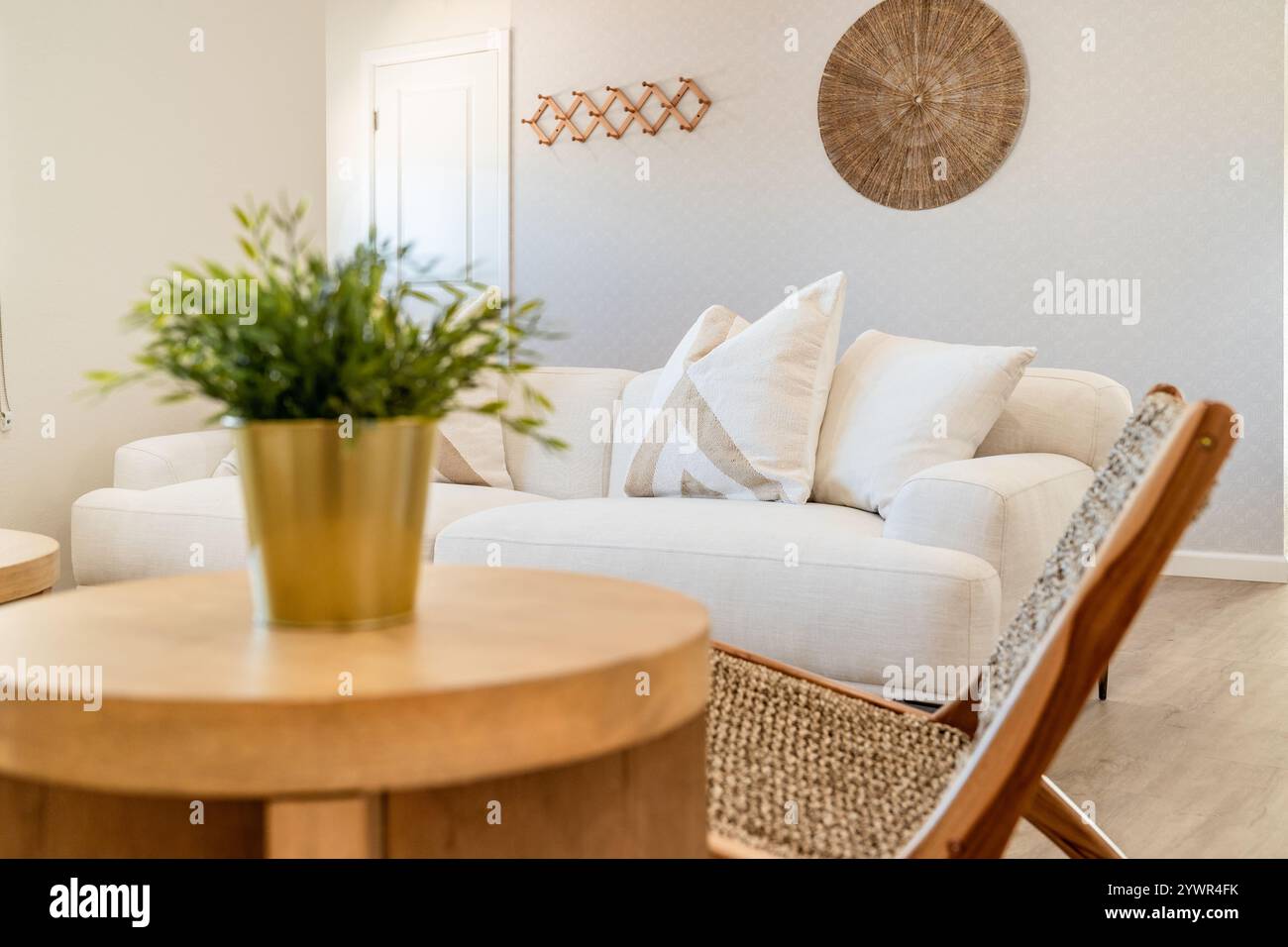 Un soggiorno nel deserto di colore chiaro presenta un divano di lino bianco con cuscini beige, un tavolino in legno e una sedia in tessuto. Foto Stock