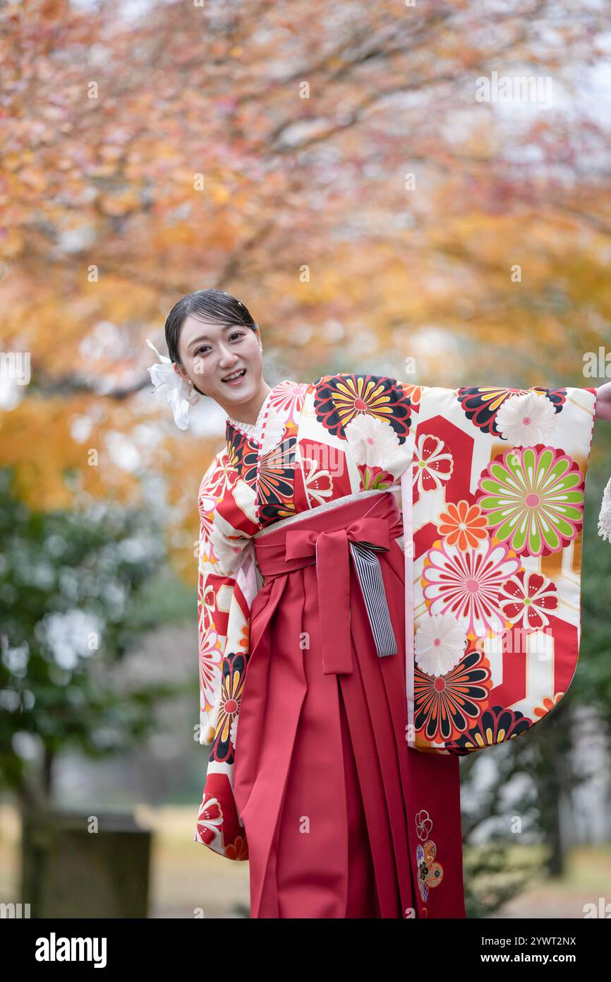 Una donna giapponese di 20 anni che indossa un kimono rosso (hakama), un punto fermo per i laureati universitari giapponesi, cammina in un tradizionale parco giapponese con la sua bellezza Foto Stock