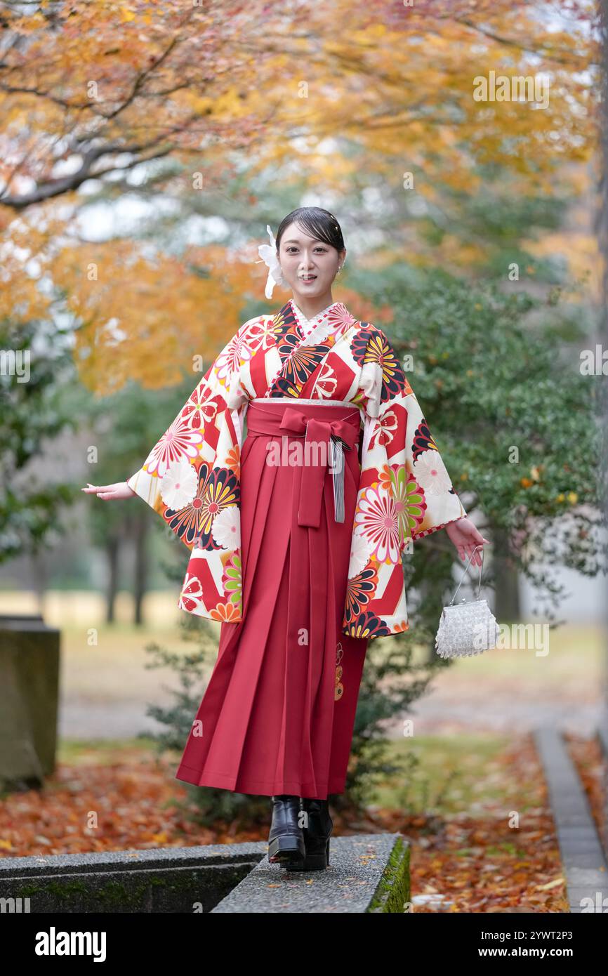 Una donna giapponese di 20 anni che indossa un kimono rosso (hakama), un punto fermo per i laureati universitari giapponesi, cammina in un tradizionale parco giapponese con la sua bellezza Foto Stock