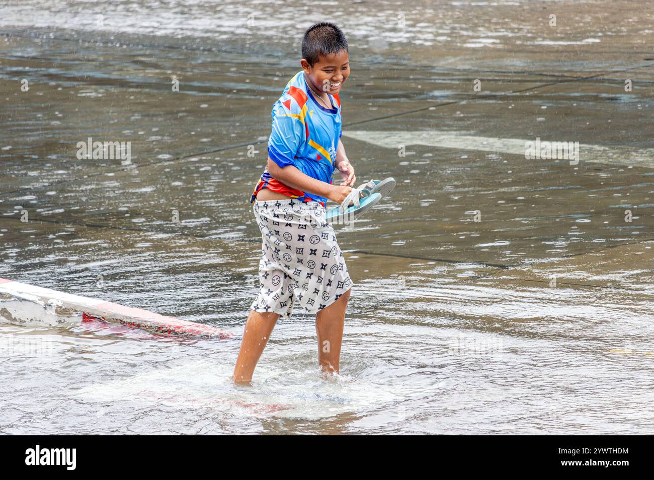 SAMUT PRAKAN, TAILANDIA, 25 2024 settembre, Un ragazzo allegro naviga su un cartellone su una pozzanghera in città Foto Stock