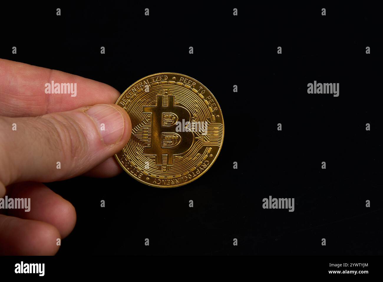 Nell'immagine, qualcuno sta afferrando un bitcoin d'oro lucido con le dita. Lo sfondo sembra essere fatto di legno e il bitcoin ha una canna metallica Foto Stock
