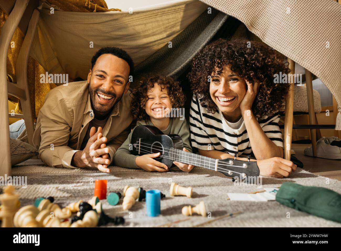 Ritratto di una famiglia allegra di tre persone trascorre del tempo di qualità all'interno di un'accogliente fortezza coperta, sorridendo e divertendosi con le attività ricreative. Foto Stock