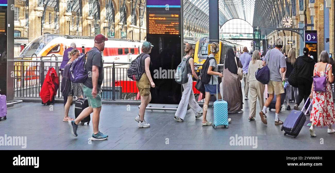 Gruppo misto di passeggeri estivi che camminano sul binario uno con valigia e bagaglio per salire a bordo del treno in partenza a Kings Cross Londra Inghilterra Regno Unito Foto Stock