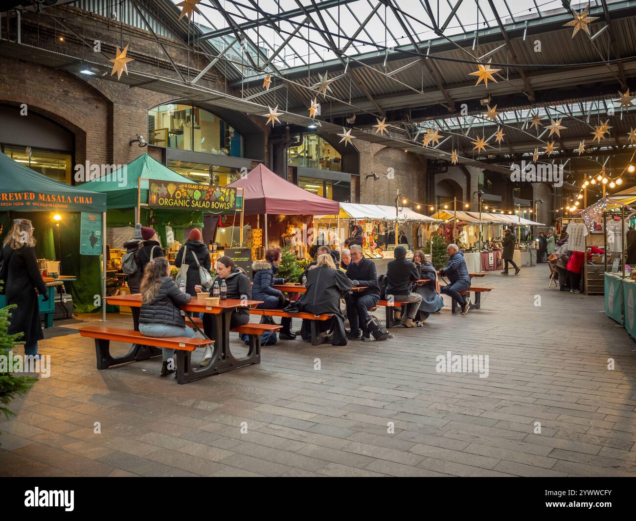 Gli amanti dello shopping apprezzano il cibo da bancarelle indipendenti seduti ai tavoli del Canopy Market di King's Cross Foto Stock