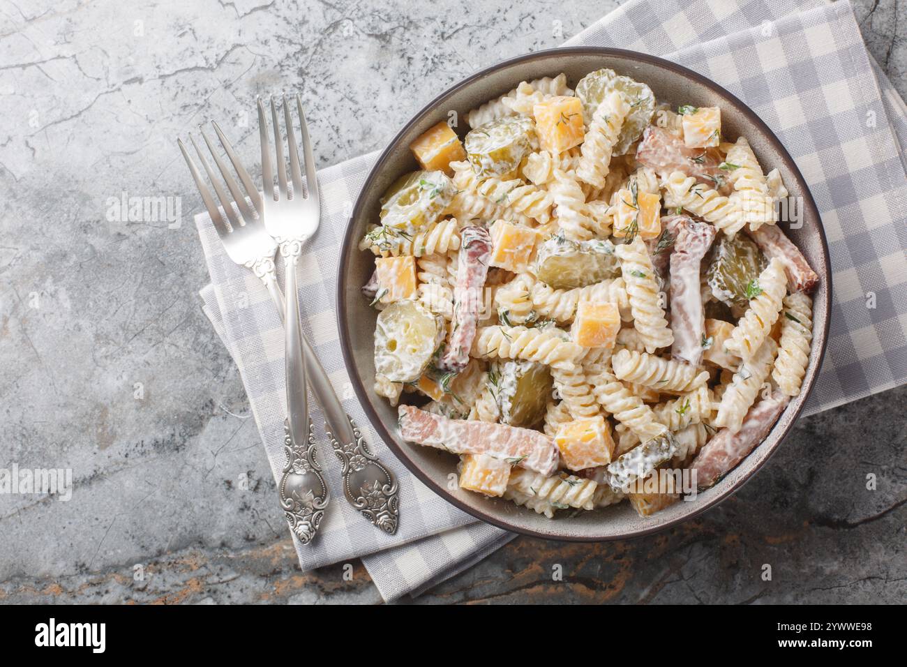 Insalata di pasta invernale deliziosa con sottaceti, formaggio giallo, erbe e pancetta condite con maionese da vicino in una ciotola sul tavolo. Via superiore orizzontale Foto Stock