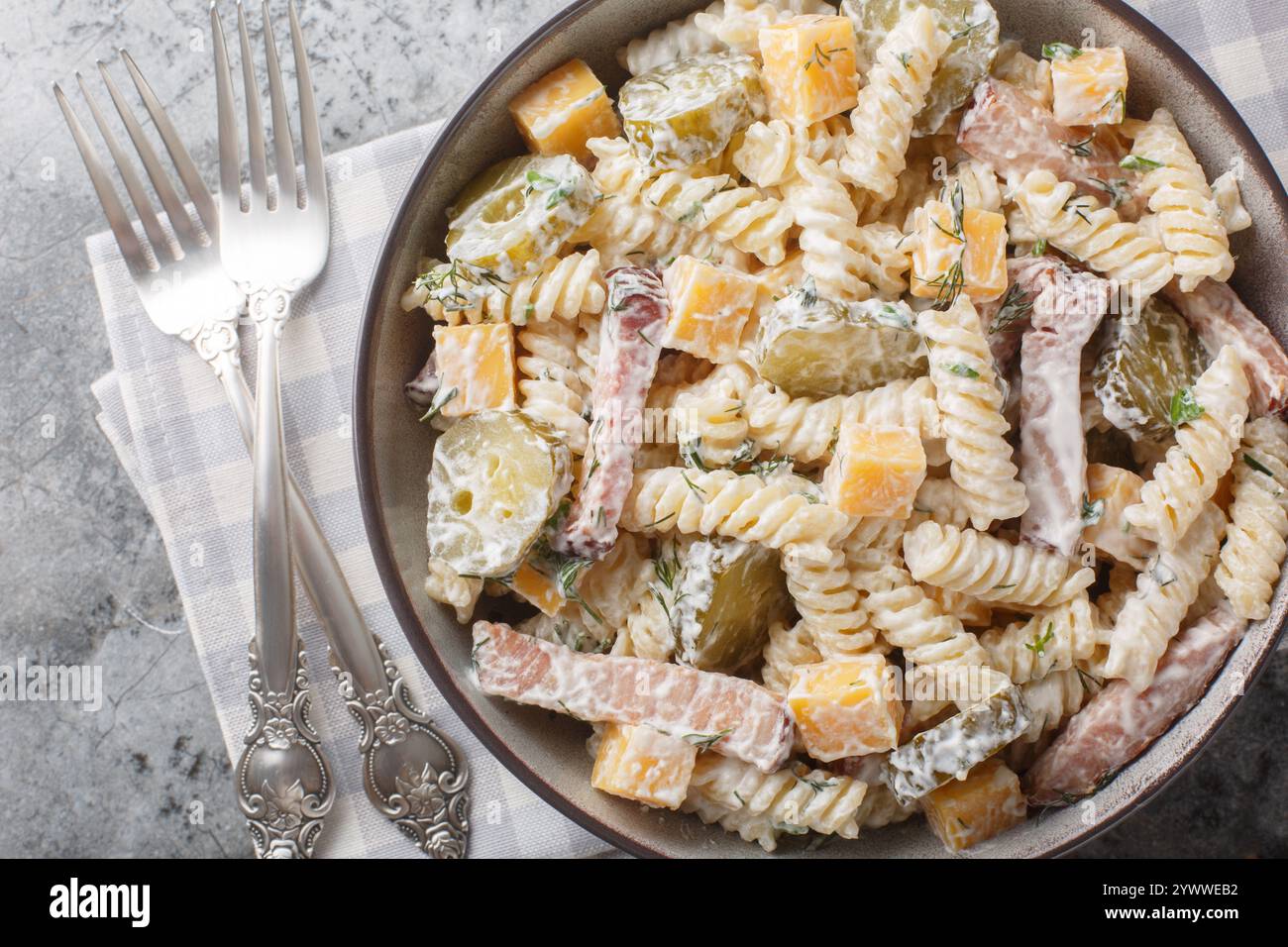 Insalata di pasta italiana Fusilli con sottaceti, formaggio giallo, aneto e pancetta condita con maionese da vicino in una ciotola sul tavolo. Vista orizzontale dall'alto f Foto Stock