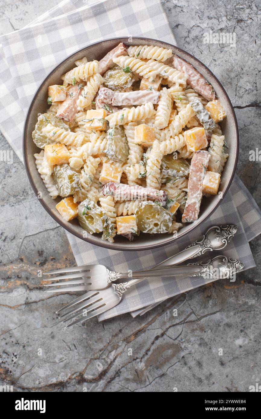 Insalata di pasta Fusilli con sottaceti, formaggio cheddar, aneto e pancetta conditi con salsa di panna da vicino nel recipiente sul tavolo. Vista dall'alto verticale Foto Stock