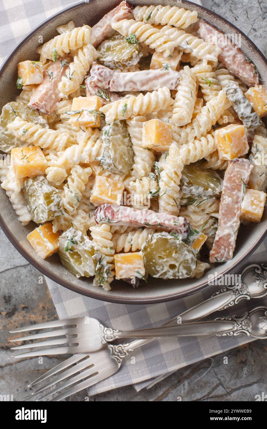 Insalata di pasta al sottaceto con formaggio cheddar, aneto e pancetta conditi con salsa di panna da vicino nel recipiente sul tavolo. Vista dall'alto verticale Foto Stock