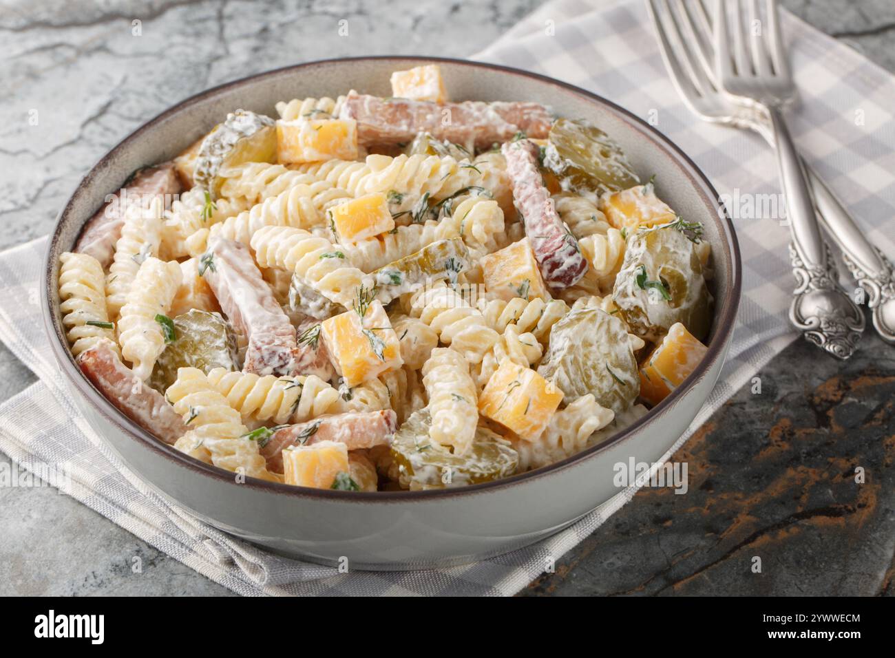 Insalata cremosa di pasta al sottaceti con formaggio giallo, erbe e pancetta in primo piano nel recipiente sul tavolo. Orizzontale Foto Stock