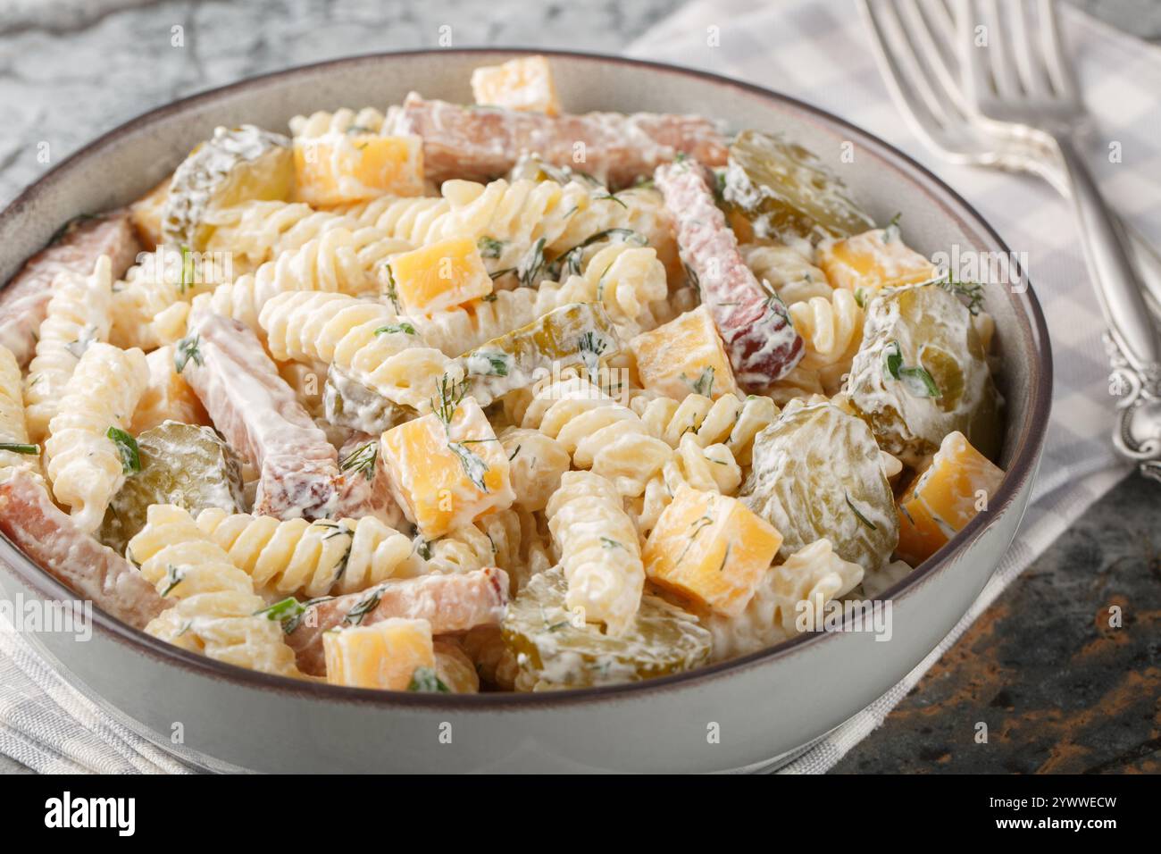 Insalata di pasta italiana Fusilli con sottaceti, formaggio giallo, aneto e pancetta condita con maionese da vicino in una ciotola sul tavolo. Orizzontale Foto Stock