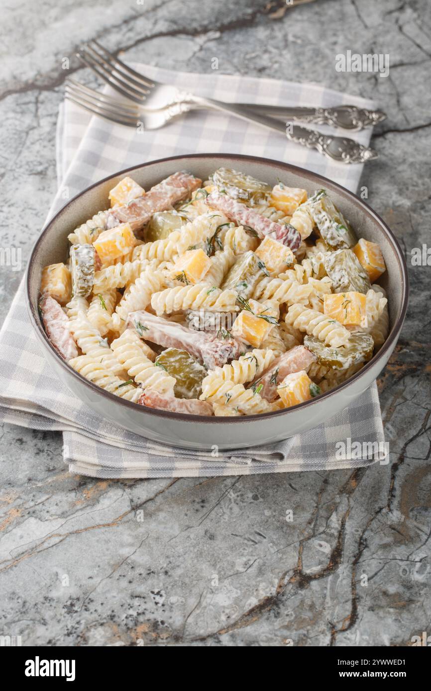 Insalata di pasta Fusilli con sottaceti, formaggio cheddar, aneto e pancetta conditi con salsa di panna da vicino nel recipiente sul tavolo. Verticale Foto Stock