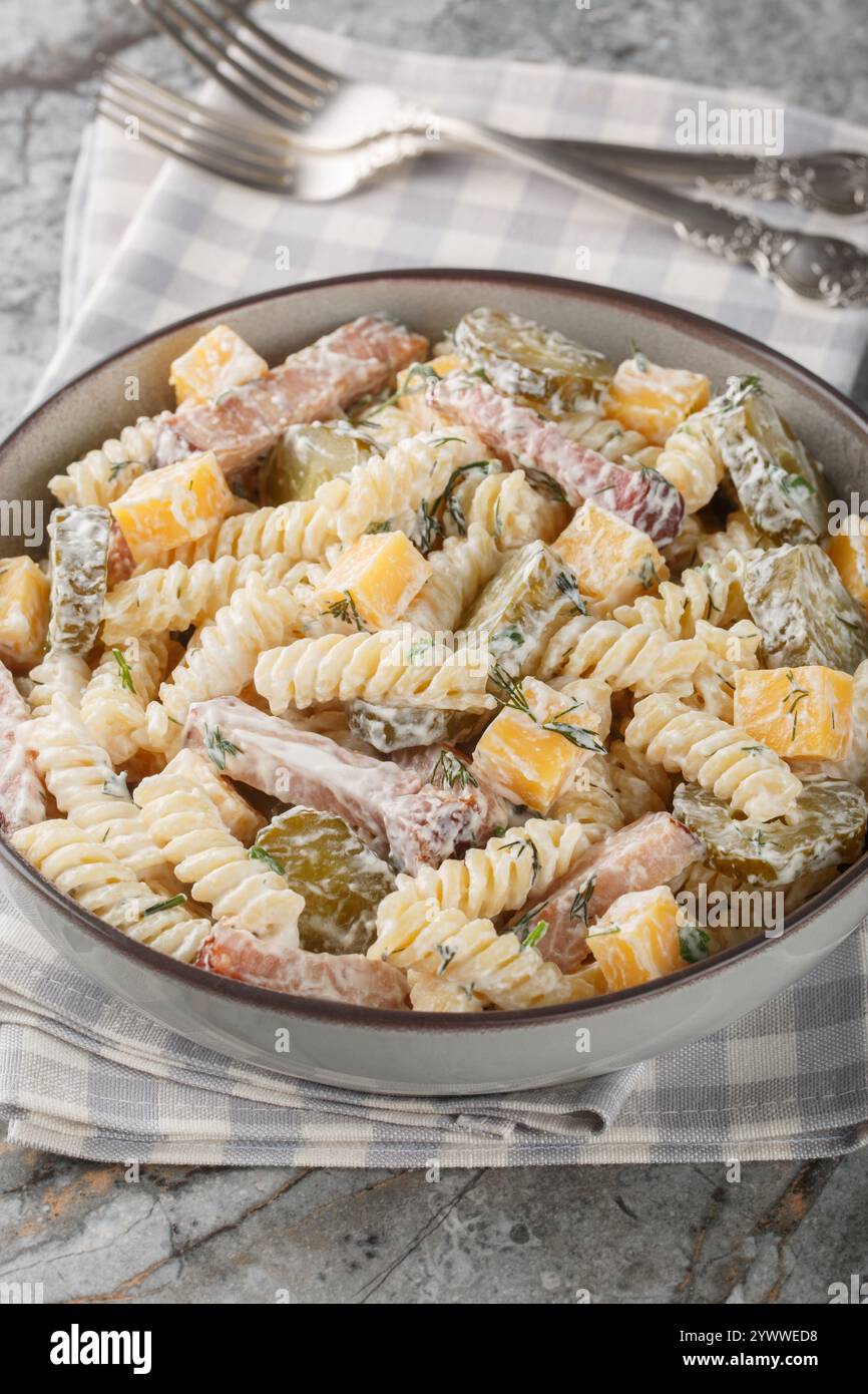Insalata di pasta al sottaceto con formaggio cheddar, aneto e pancetta conditi con salsa di panna da vicino nel recipiente sul tavolo. Verticale Foto Stock