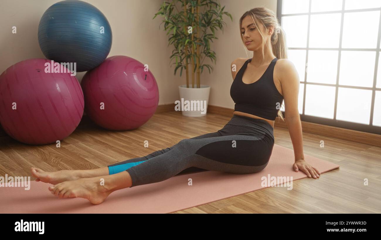 Donna che si allena su un tappetino da yoga in palestra circondata da grandi palle, indossa un abbigliamento atletico, dimostrando tecniche di fitness e relax Foto Stock
