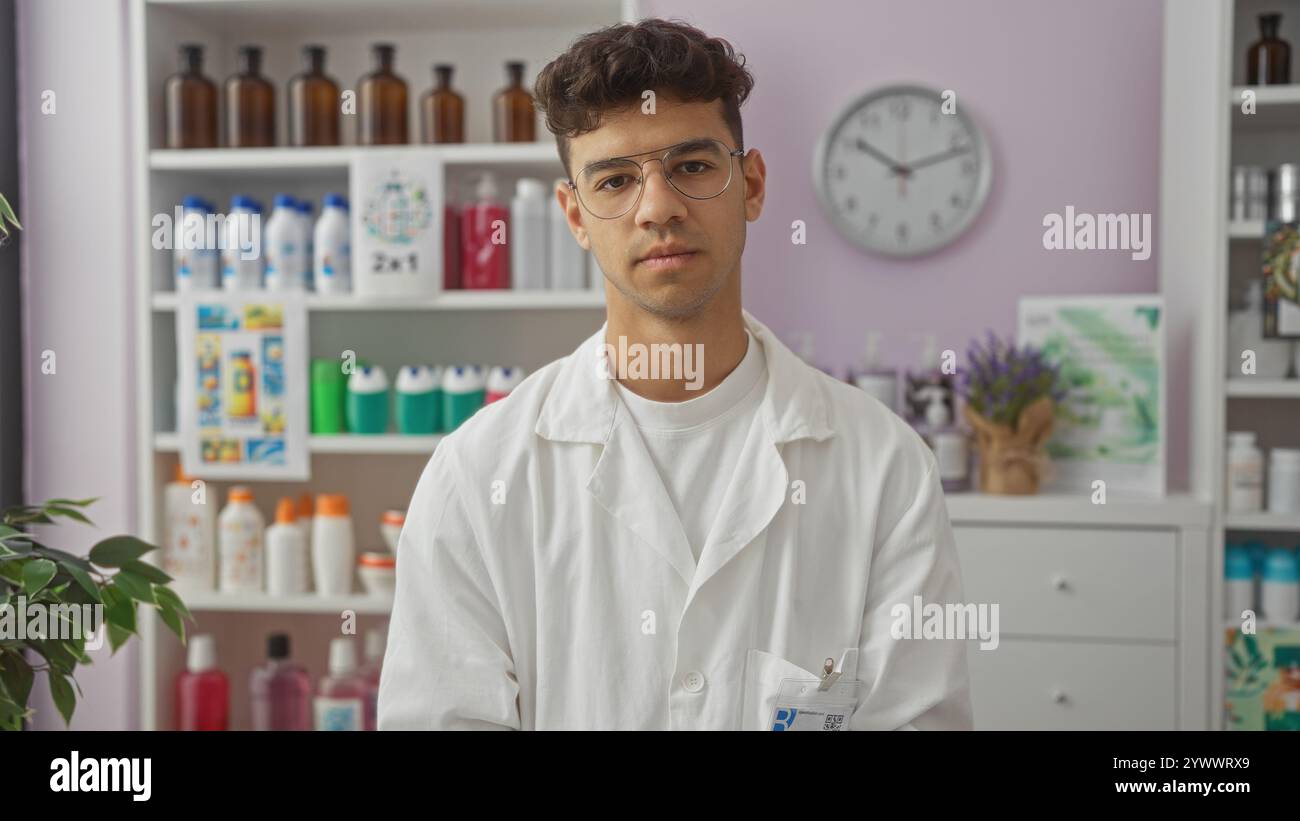 Giovane ispanico in un camice bianco in piedi in una farmacia con scaffali di prodotti dietro di lui, tra cui bottiglie di vari articoli, una pianta e un Foto Stock