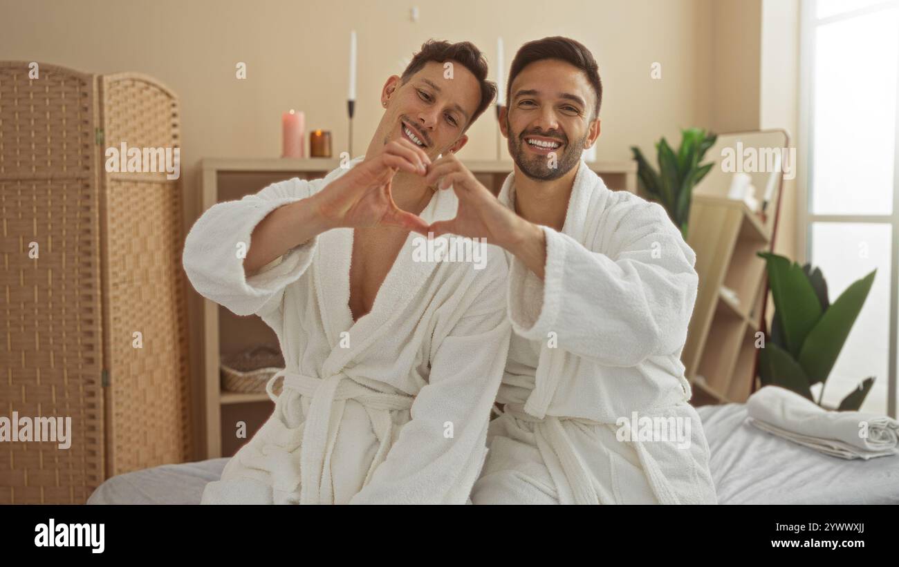 Coppia di uomini che indossano abiti bianchi a forma di cuore con le mani in una spa, godendosi un momento rilassante all'interno, rappresentando l'amore e lgbtq com Foto Stock