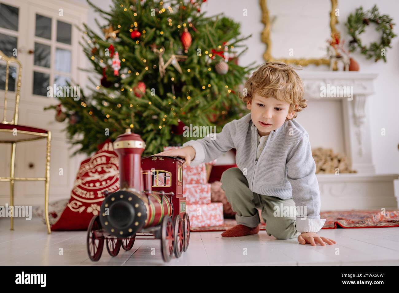 Scena natalizia natalizia con un bambino che gioca con un treno giocattolo vicino a un albero splendidamente decorato Foto Stock