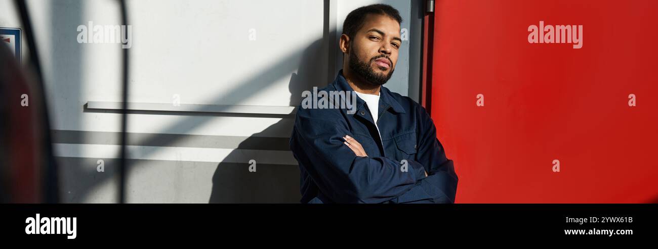 Il bellissimo giovane meccanico si appoggia contro un muro, mostrando abilità e determinazione nel suo lavoro. Foto Stock