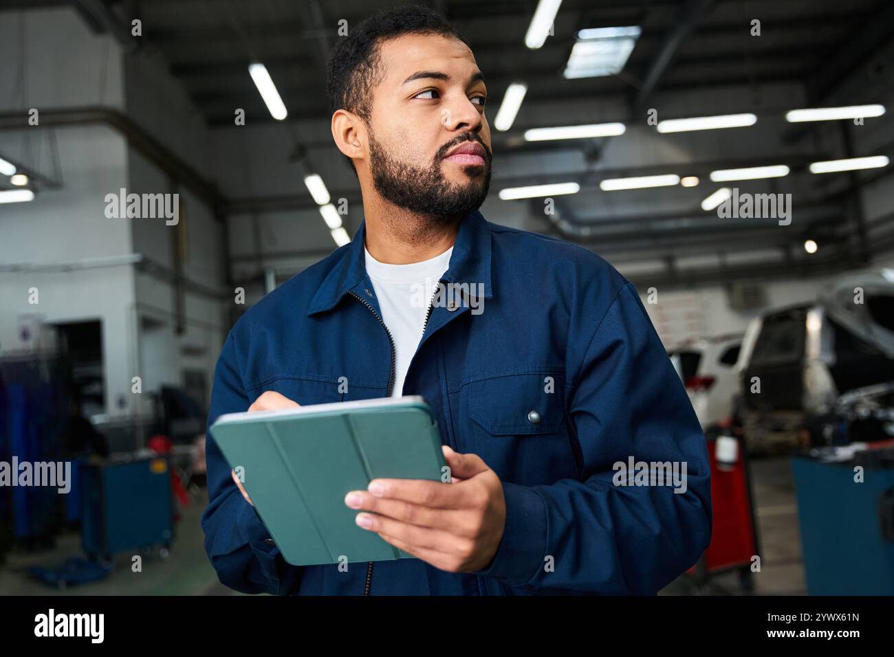 Il giovane meccanico rivede il suo programma di lavoro in una moderna officina di riparazione automobilistica. Foto Stock