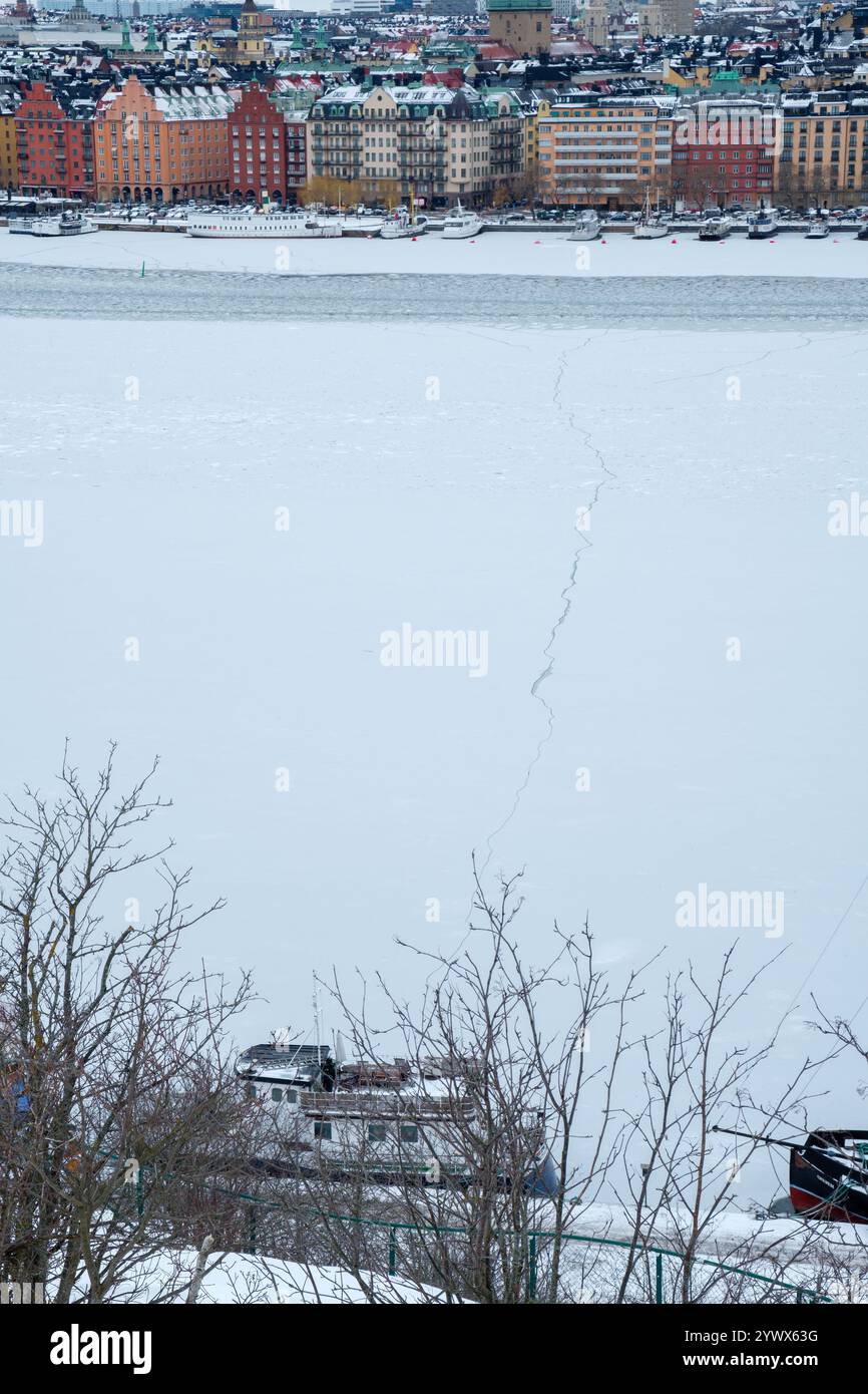 La neve copre il paesaggio di Stoccolma, mentre un fiume ghiacciato riflette edifici colorati. La fredda aria invernale aggiunge un fascino sereno e invitante alla scoperta. Foto Stock