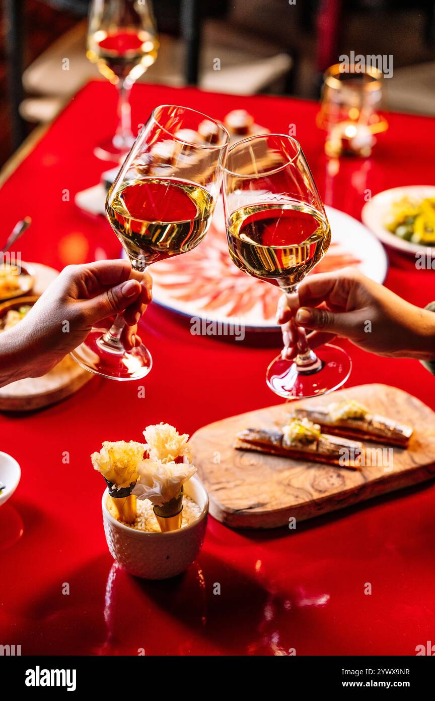 Due mani stringono i bicchieri di vino bianco durante una cena romantica. Foto Stock