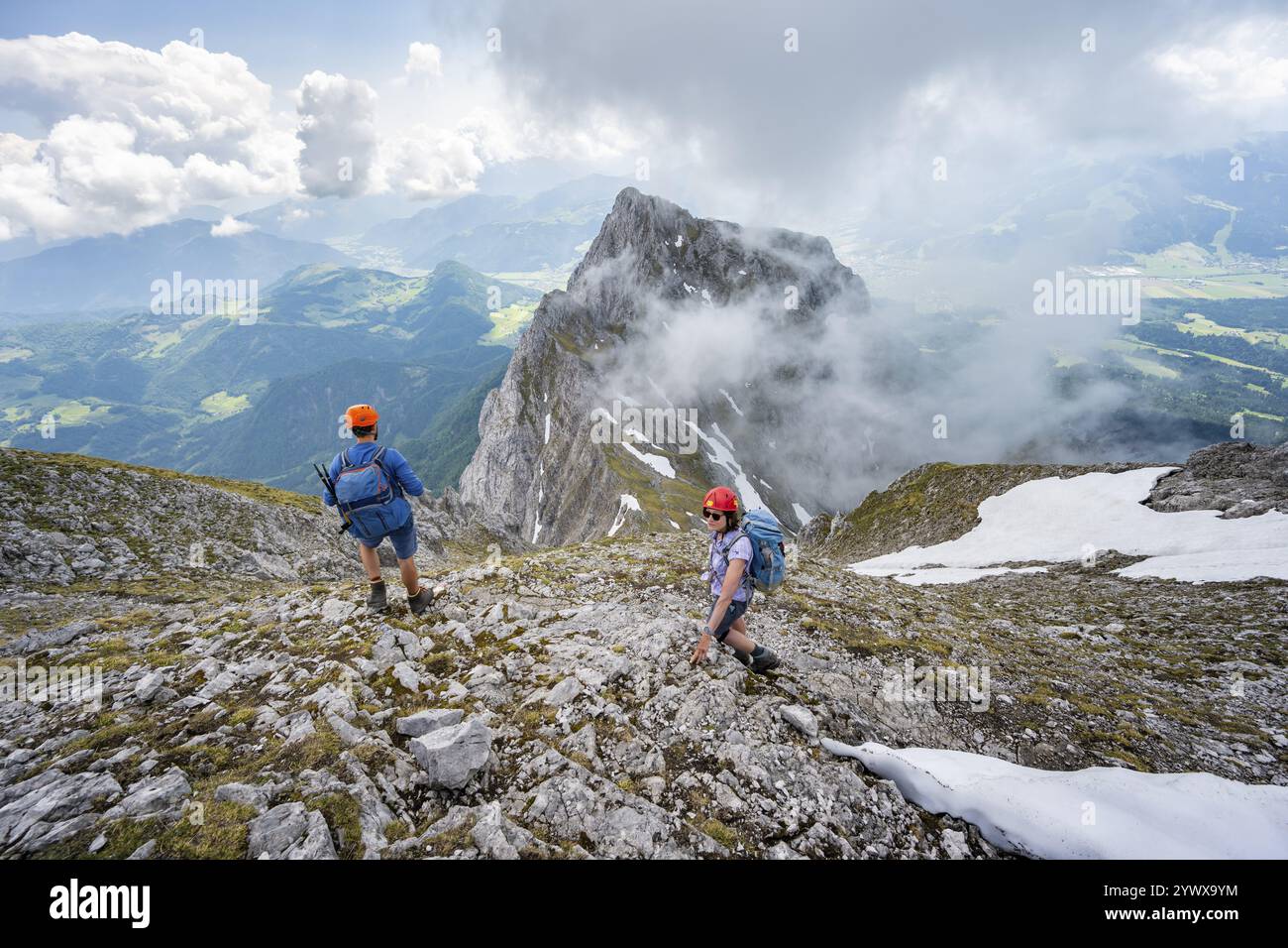 Alpinista con casco su uno stretto sentiero escursionistico, ascesa all'Ackerlspitze, nuvole che si muovono intorno alle montagne, Wilder Kaiser, Kaiser Mountains, Tyr Foto Stock