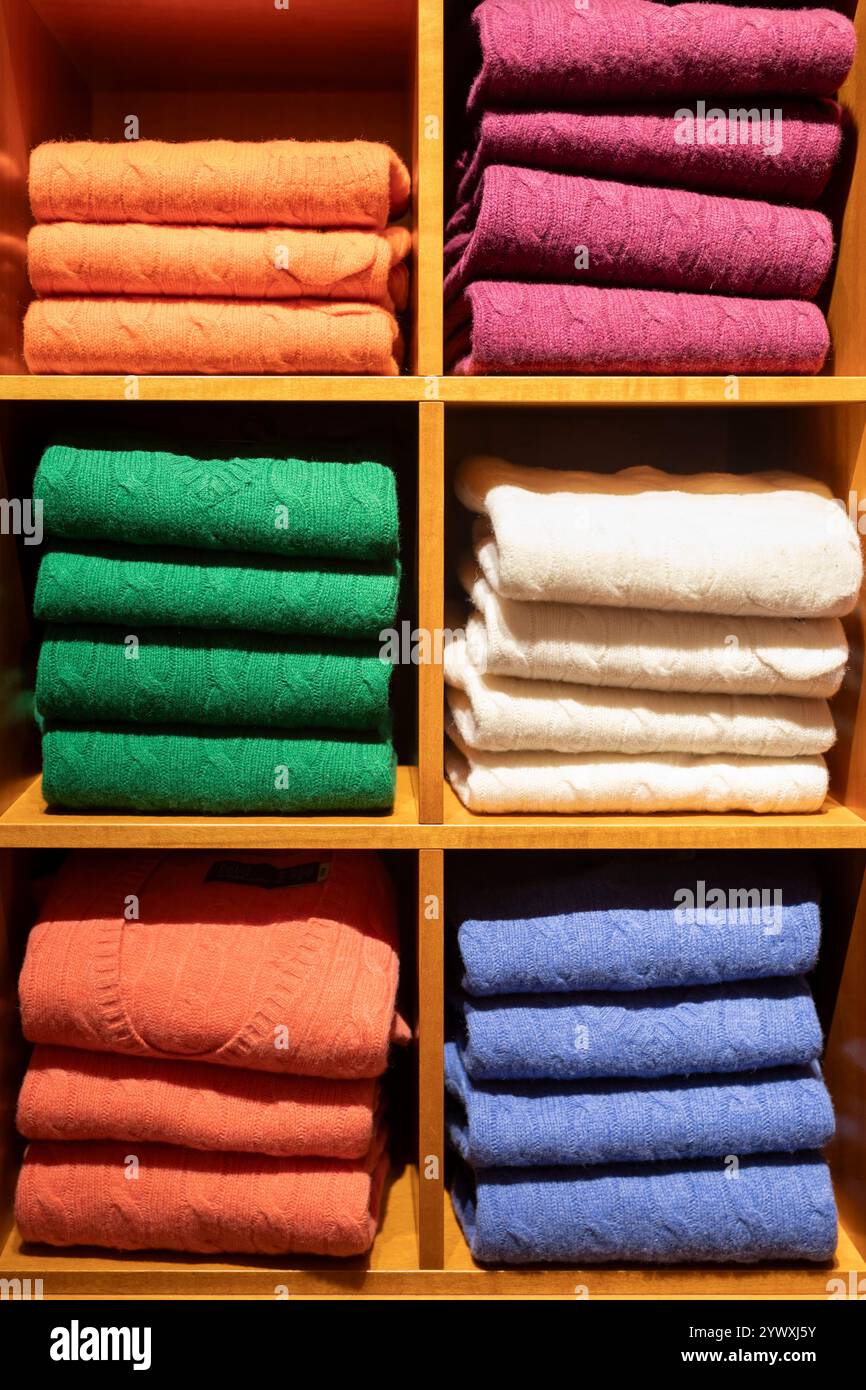 I pullover in lana e cashmere dai colori vivaci con motivi a maglia a cavo sono impilati in modo ordinato dal colore in un guardaroba. Foto Stock